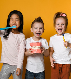Three children smiling and holding oversized brushes and mouth mold