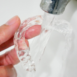 A person cleaning their Invisalign aligners with water